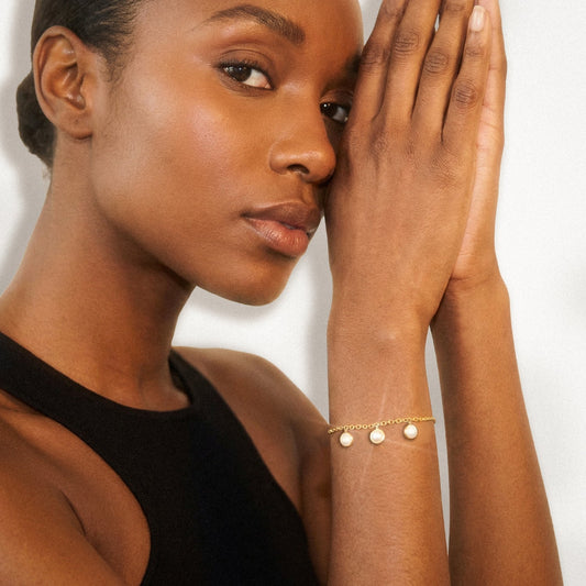 Woman wearing a gold bracelet with three pearl charms on a plain background