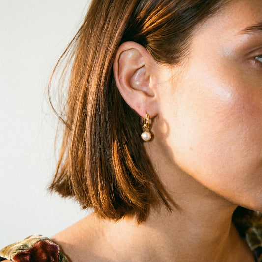 Close-up of a person wearing a pearl earring with a neutral background