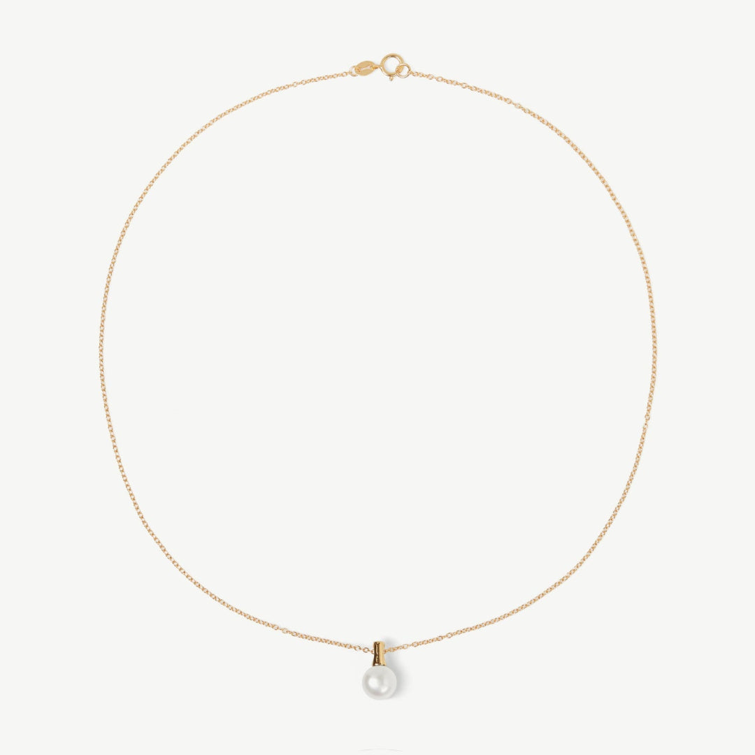 Gold necklace with a pearl pendant on a light beige background