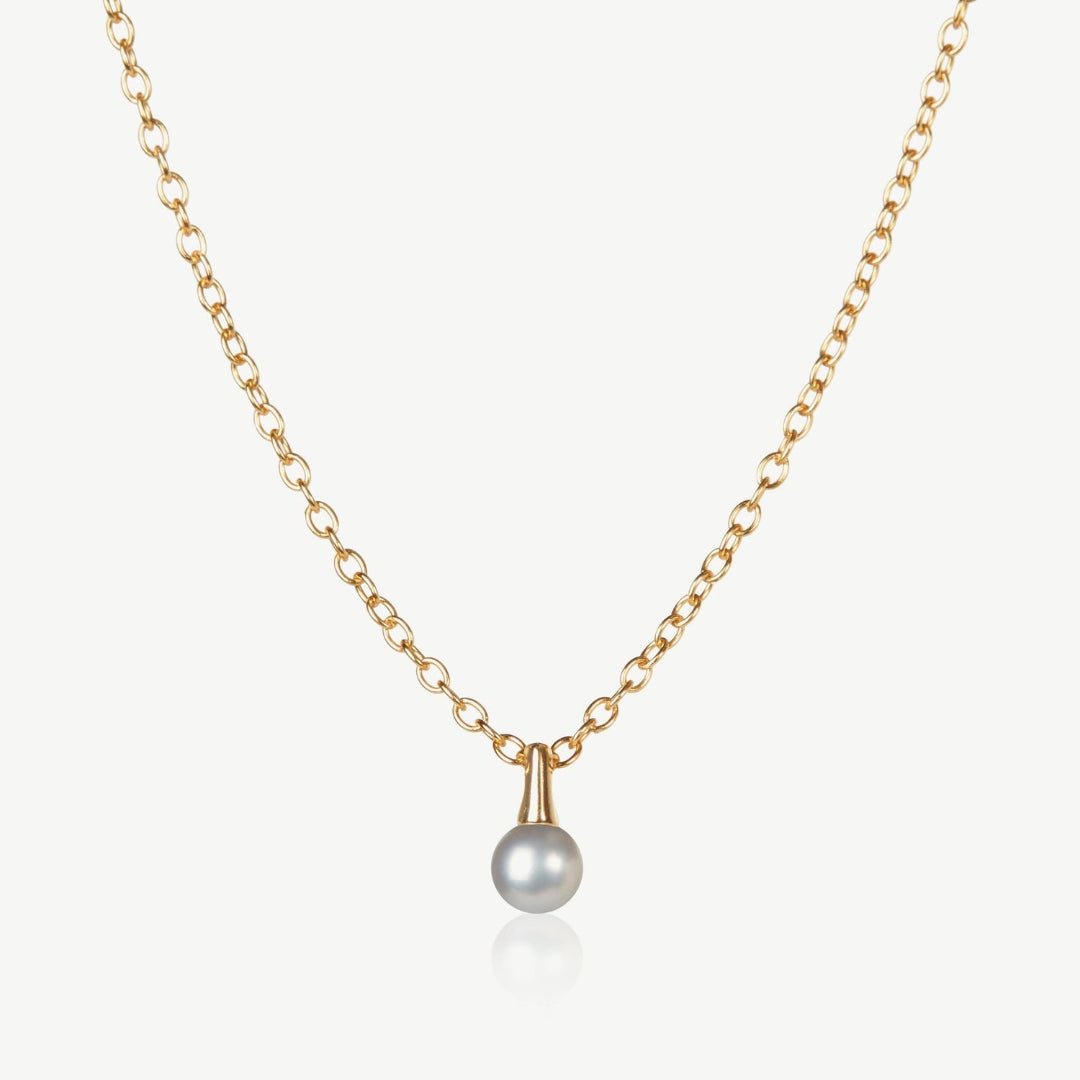 Gold necklace with a single pearl pendant on a light beige background