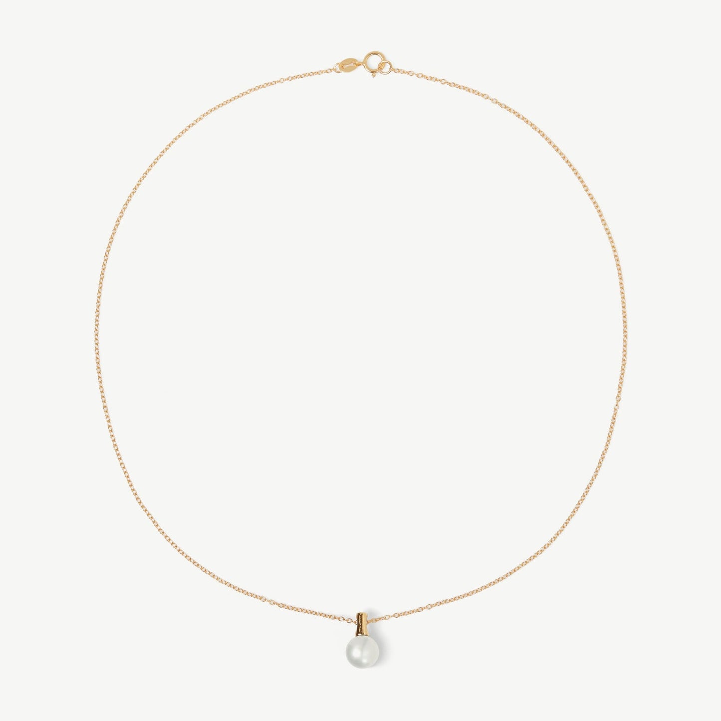 Gold necklace with a single pearl pendant on a light beige background