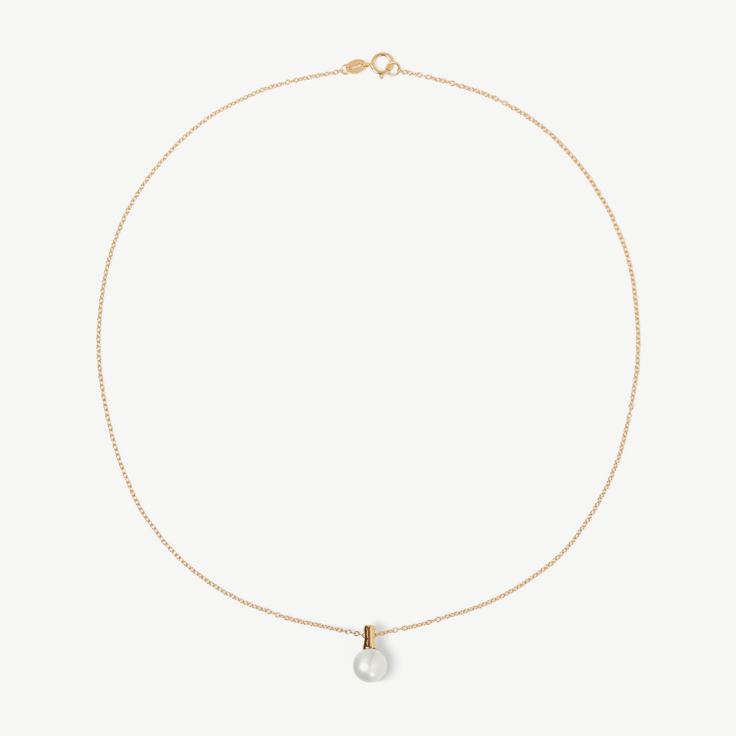 Gold necklace with a single pearl pendant on a light beige background