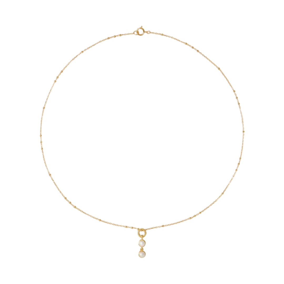 Gold necklace with a small pendant on a light beige background