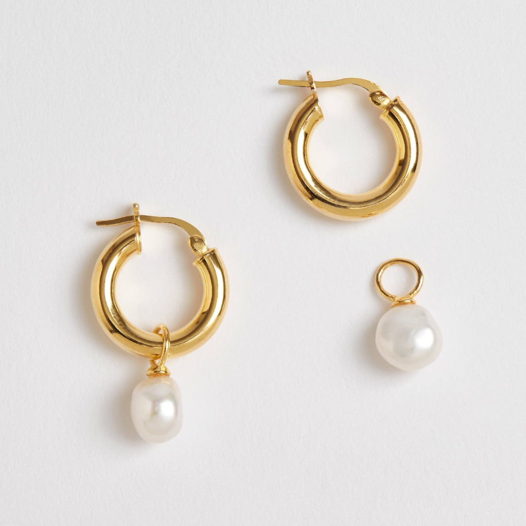 Gold hoop earrings with pearl drops on a light gray background