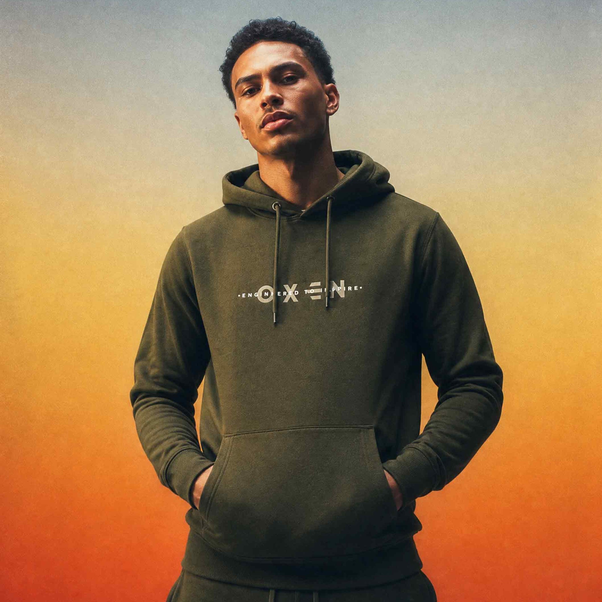 Man wearing a green hoodie with a brand logo against an orange and blue gradient background