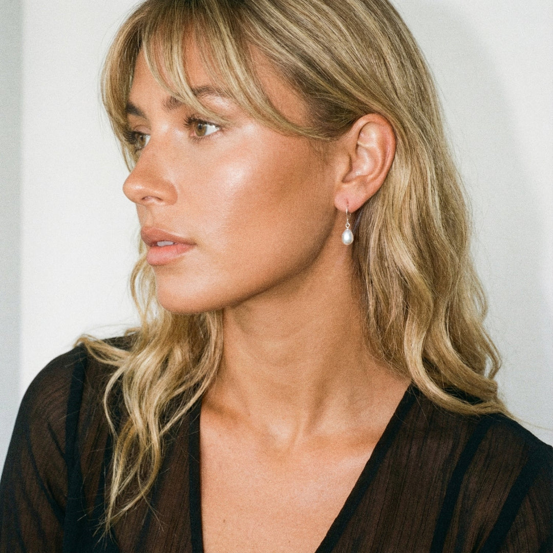 Woman wearing a pearl earring against a plain background