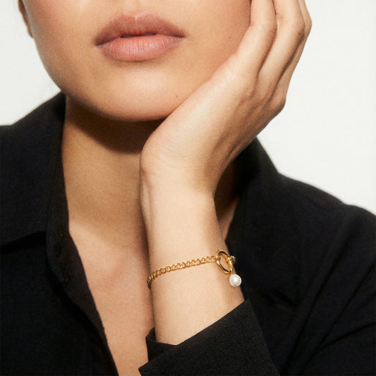 Woman wearing a gold bracelet with a pearl charm, against a neutral background