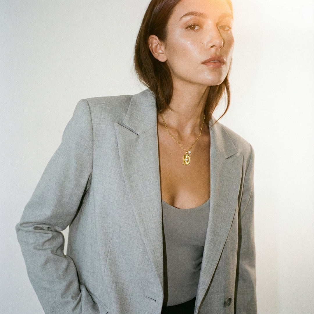 Woman wearing a gray blazer over a plain top with a blurred background