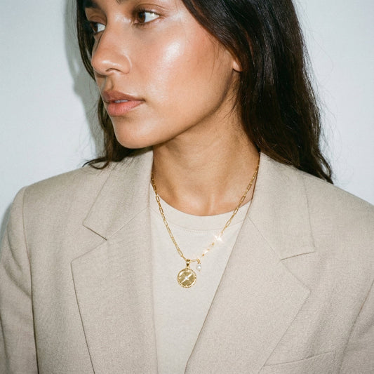 Woman wearing a beige blazer and gold necklace against a plain background