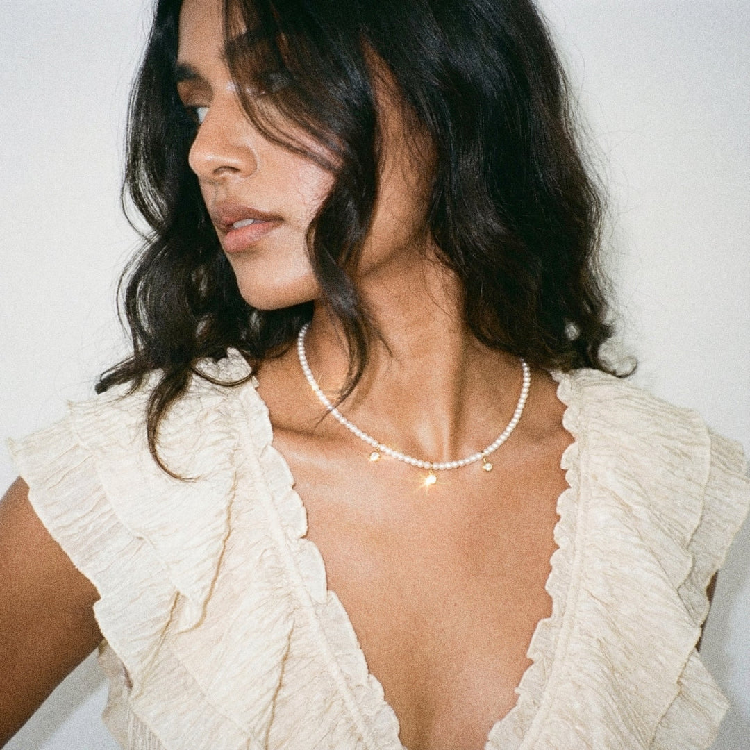 Woman wearing a pearl necklace with a white textured top against a neutral background